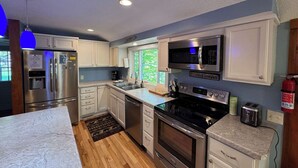 A modern kitchen with stainless steel appliances, white cabinetry, and a large window providing natural light.