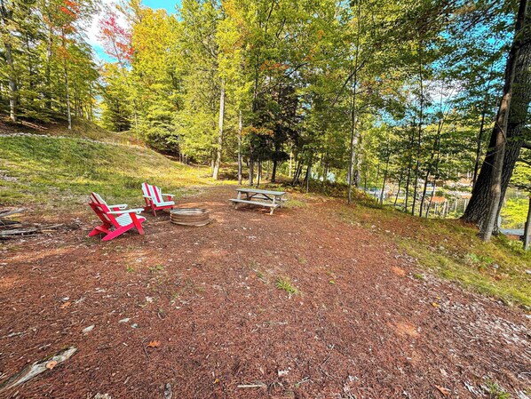 Ein Campingplatz mit zwei roten Adirondack-Stühlen, einem Picknicktisch und einer Feuerstelle.