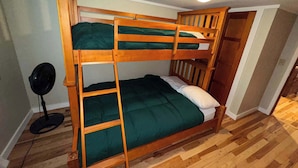 A bunk bed room with a ladder, a fan, and a door leading to another room.