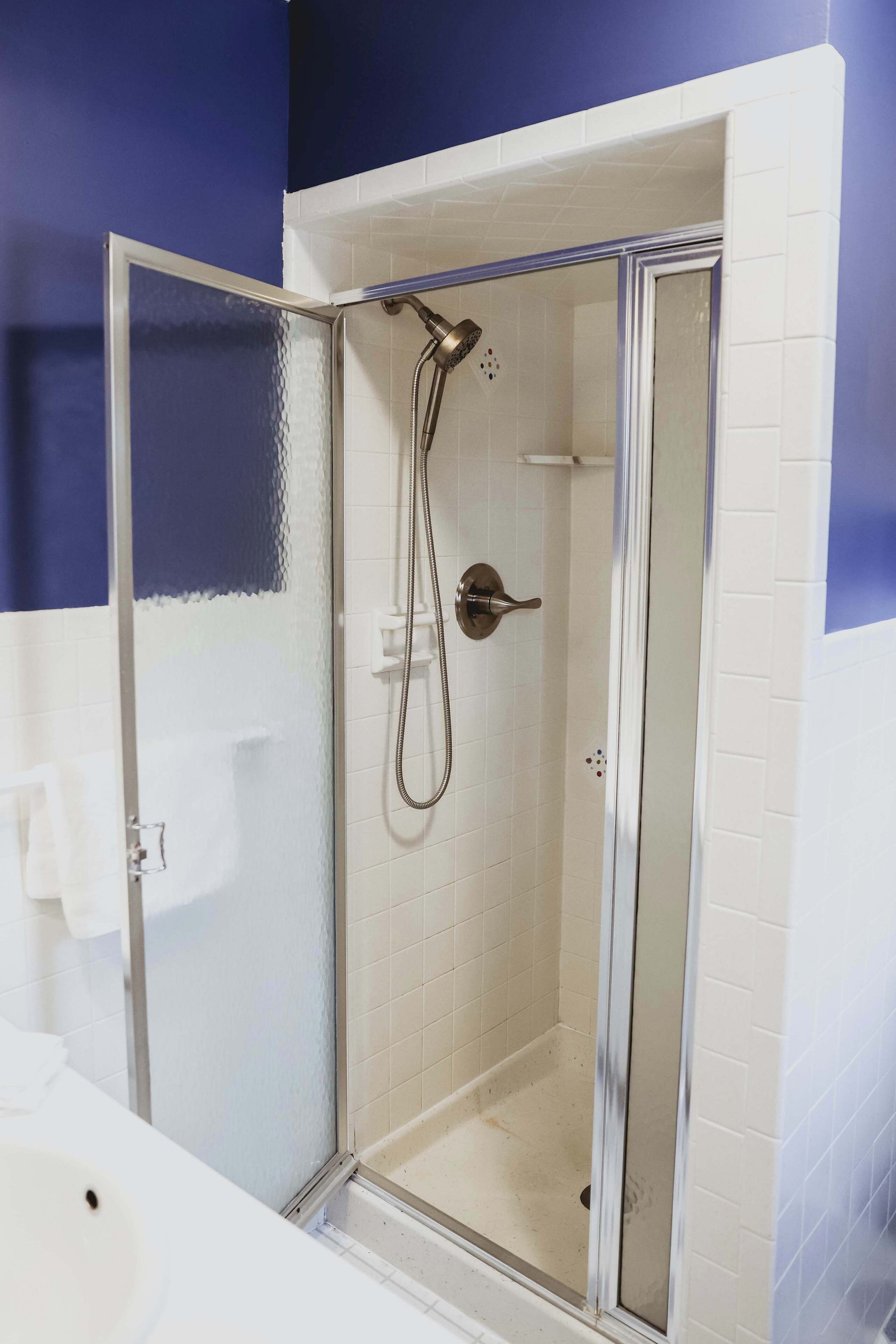 A glass-enclosed shower with a handheld showerhead and a wall-mounted faucet.