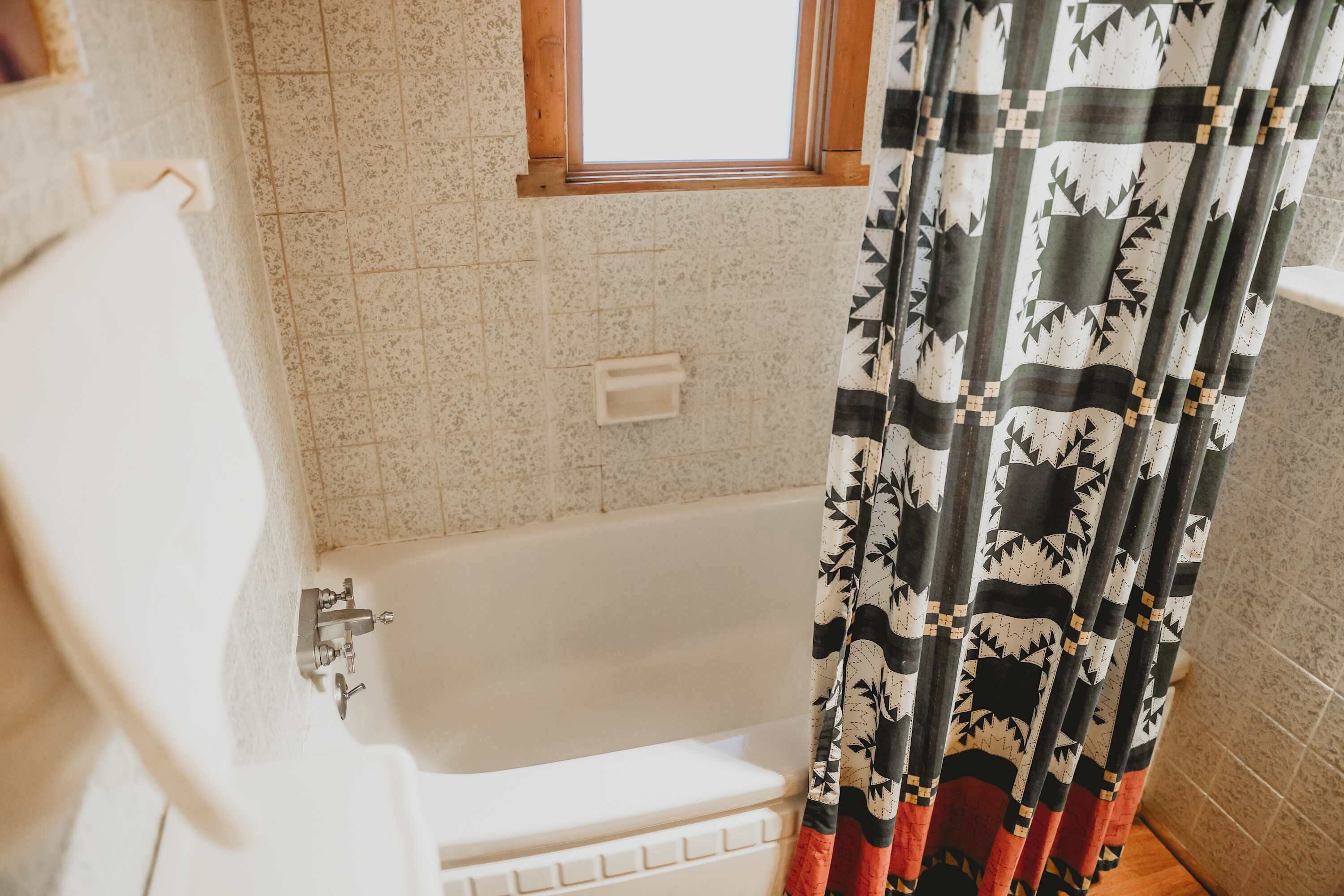 A bathroom with a bathtub, a window, and a patterned shower curtain.