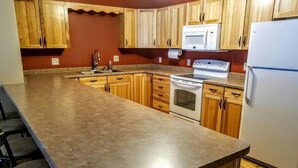 A kitchen with wooden cabinets, a granite countertop, a stainless steel sink, a white stove, and a white refrigerator. - Minocqua Lake Condo B10 (Minocqua)