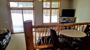 A cozy living room with a wooden staircase, a black leather sofa, a dining table with chairs, and a stone fireplace. - Minocqua Lake Condo B10 (Minocqua)