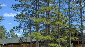 A lodge with a wooden deck extending over a lake, surrounded by tall pine trees. - Minocqua Lake Condo B10 (Minocqua)