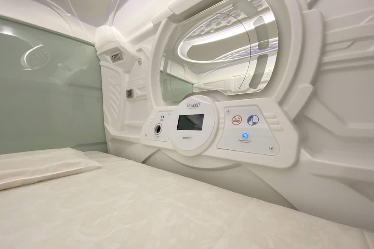 Une pièce moderne et bien éclairée, équipée d’un panneau de commande pour un appareil de massage, d’un lit recouvert d’un tissu à motifs et d’une cloison en verre.