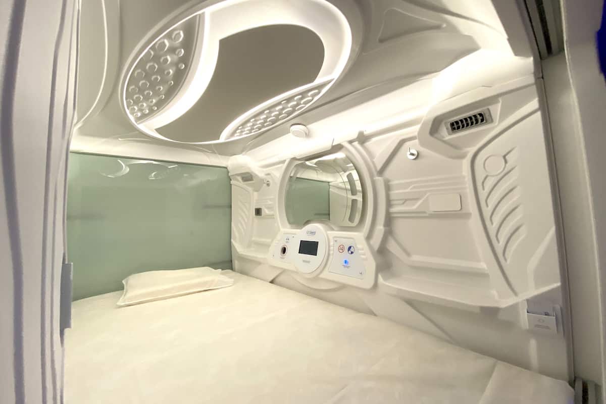Une pièce moderne et bien éclairée, équipée d’un lit, d’un panneau de commande et d’une fenêtre circulaire.