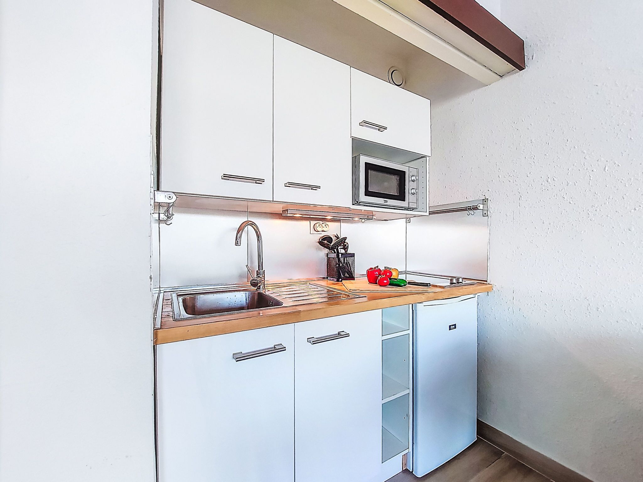 A compact kitchen with white cabinets, a stainless steel sink, a microwave, and a small refrigerator.
