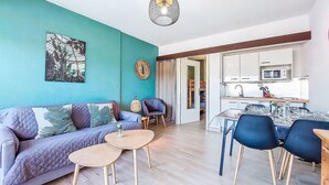 A modern living room with a teal accent wall, a sofa, two small round tables, and a dining area with chairs.