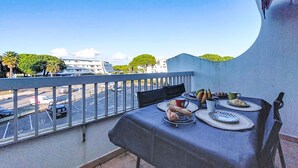 A balcony with a table set for dining, overlooking a street with parked cars and buildings.