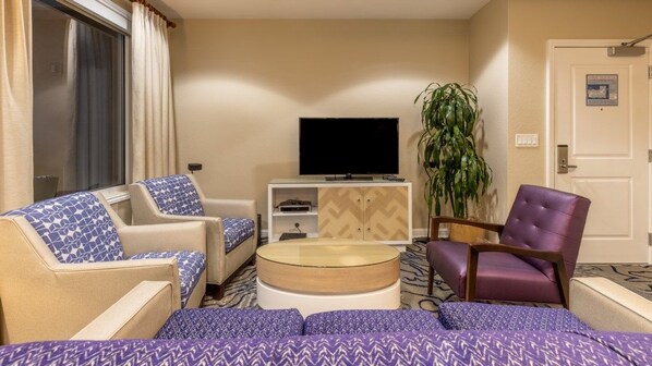 Une chambre d’hôtel comprenant un canapé, un téléviseur, une table basse et un fauteuil violet.