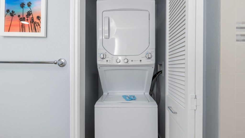 A compact laundry room with a washer and dryer, a door with a handle, and a framed picture on the wall.