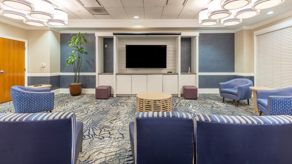 A hotel room with a flat-screen TV, a potted plant, and a seating area with chairs and ottomans.