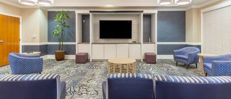 A hotel room with a flat-screen TV, a potted plant, and a seating area with chairs and ottomans.