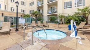 Un bain à remous entouré de chaises longues et un espace au bord de la piscine avec un panneau indiquant une zone de spa et les précautions à prendre.