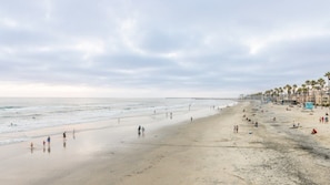 Una playa extensa con gente caminando y nadando, palmeras y edificios a lo largo de la orilla.