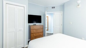 Une chambre à coucher comprenant un lit, une commode en bois, un téléviseur et une porte donnant sur une autre pièce.