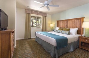 A hotel room with a bed, a TV, a wooden nightstand, a lamp, a ceiling fan, and a window with curtains.