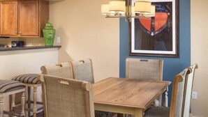 A dining area with a wooden table and chairs, a hanging light fixture, and a framed picture on the wall.