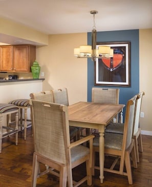 A dining area with a wooden table and chairs, a hanging light fixture, and a framed picture on the wall.