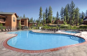 A swimming pool with lounge chairs and a wooden building in the background.