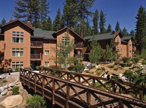 A multi-story lodge with a wooden exterior, balconies, and a wooden bridge leading to the entrance.