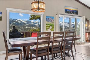 A dining area with a wooden table and chairs, large windows with mountain views, and a chandelier. - Destiny Family Vacation Home at Windcliff by RedAwning (Estes Park)
