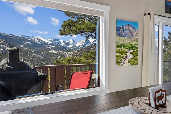 A room with a large window overlooking a mountainous landscape, a red chair, and a framed picture on the wall. - Destiny Family Vacation Home at Windcliff by RedAwning (Estes Park)