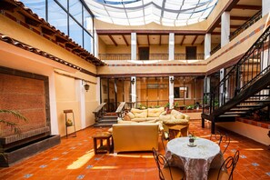 Amplio espacio interior con techo alto, una escalera y una zona de estar con sofás y una mesa.
