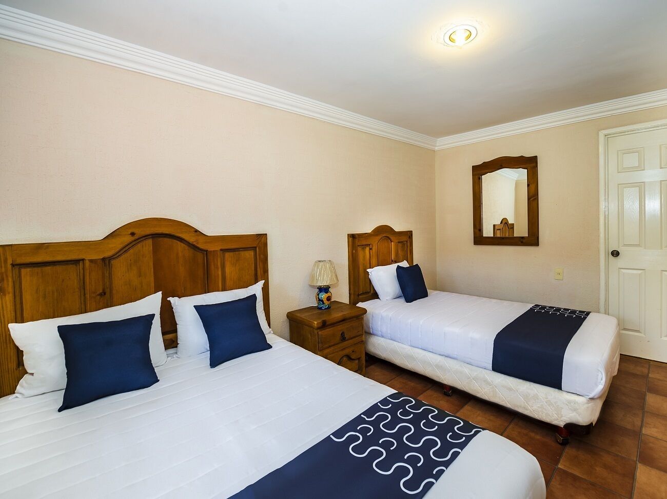 A hotel room with two beds, wooden headboards, white bedding, and a small bedside table with a lamp.