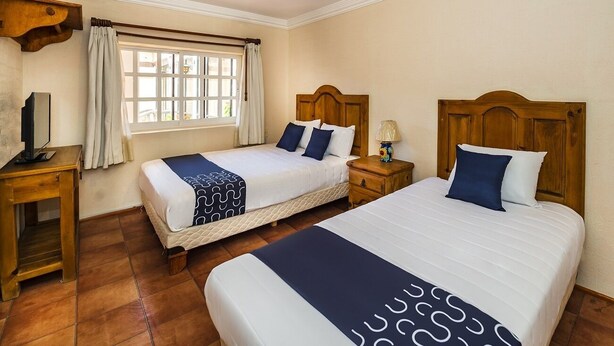 A hotel room with two beds, a wooden headboard, a bedside table with a lamp, a window with curtains, and a television on a wooden stand. - Hotel La Casa de Don Tito, Jocotitlán (Jocotitlán)