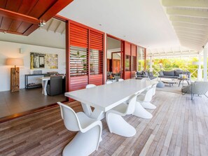 A modern dining area with a long white table, white chairs, and a red partition. - Spacious Villa Near Beach (Jan Thiel)