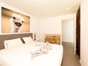 A hotel room with a large bed, a headboard, a bedside table with a lamp, a wooden cabinet, and a door with blinds. - Spacious Villa Near Beach (Jan Thiel)