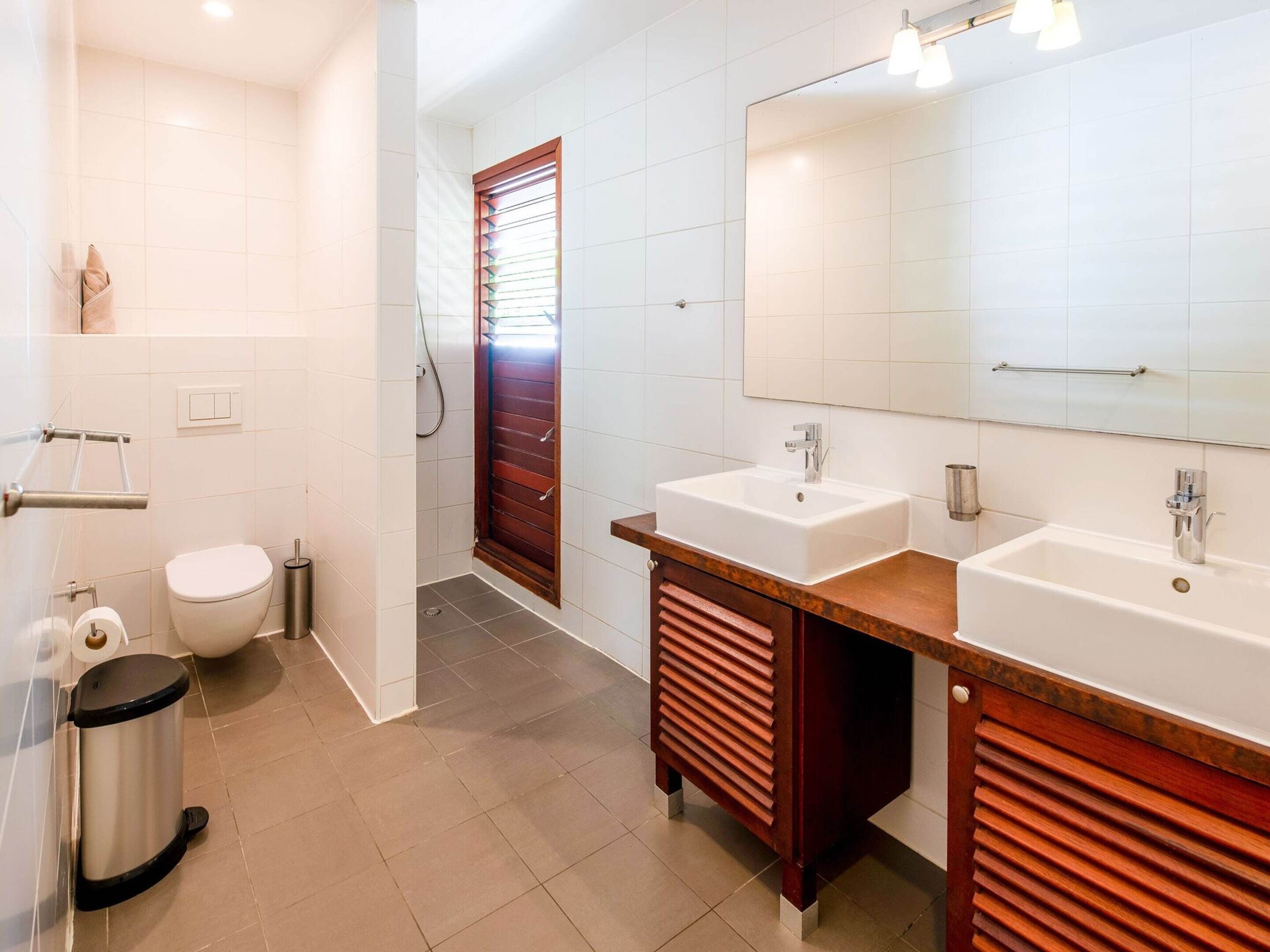A modern bathroom with two sinks, a toilet, and a shower.