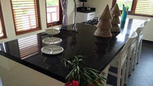 A kitchen island with a black countertop, a three-tiered cake stand, and a potted plant with pink flowers. - Magnificent Villa near Beach in Upscale District of Vista Royal, Jan Thiel (Jan Thiel)