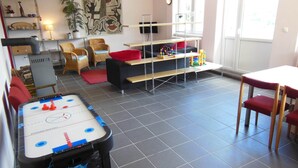 Ein Wohnzimmer mit Fußballtisch, Fernseher, Bücherregal und einem Fenster mit Tageslicht.