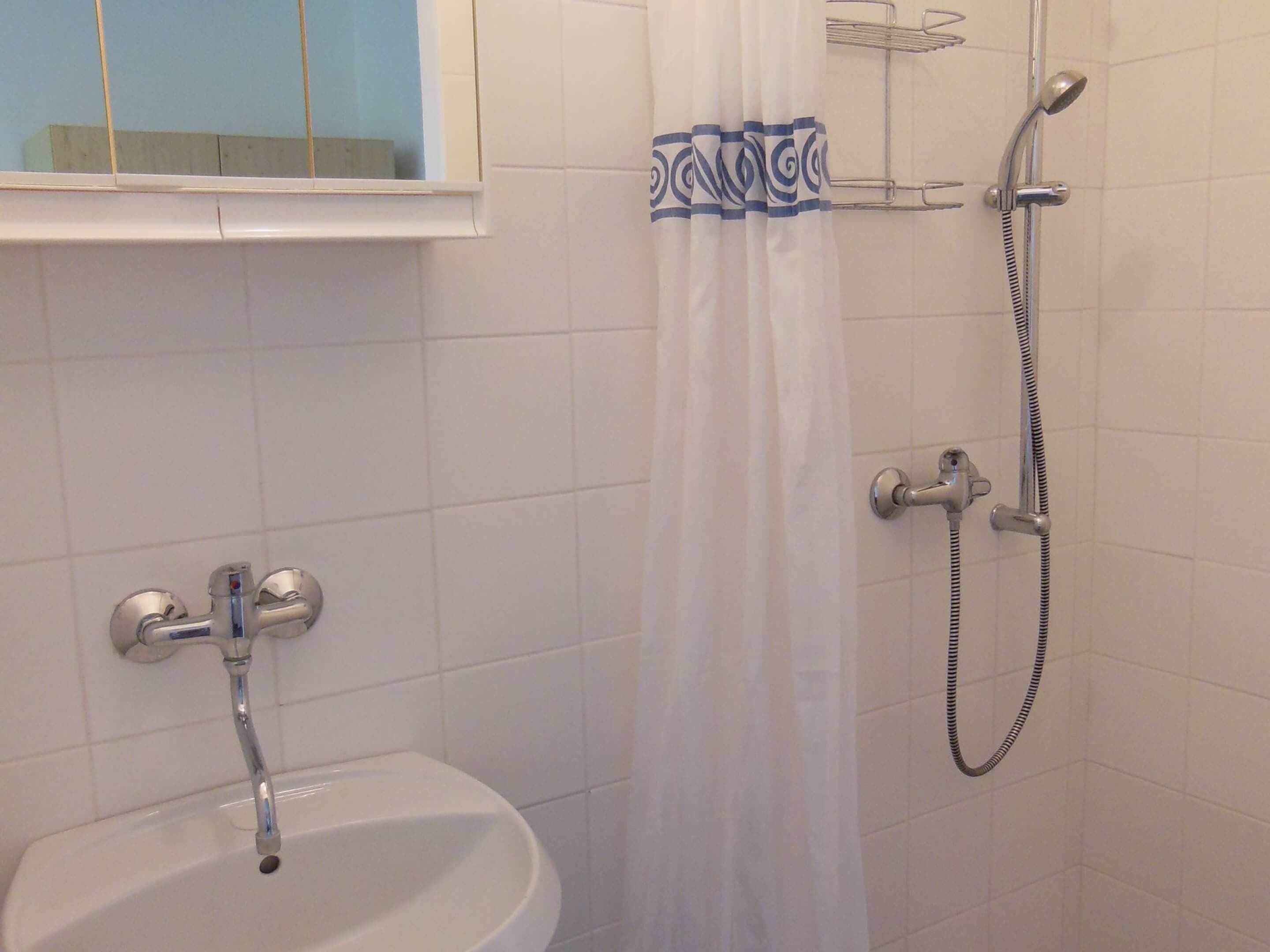 Un baño con lavamanos, ducha y ventana con cortina.
