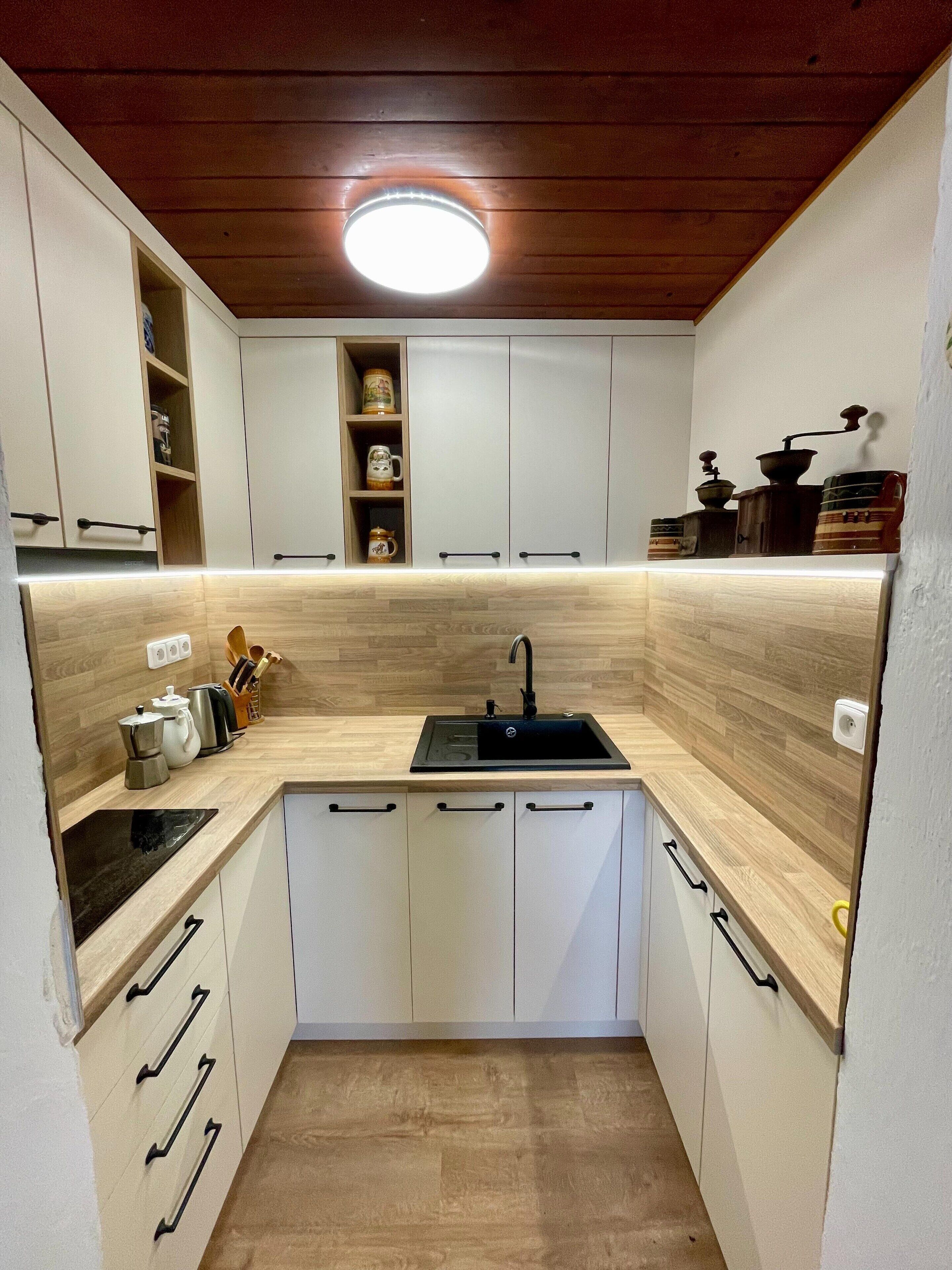 Una cocina compacta con armarios blancos, un lavamanos negro y encimeras de madera.