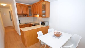 Une cuisine compacte avec des meubles en bois, un four à micro-ondes et un coin repas comprenant une table et des chaises blanches.