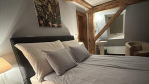 Un dormitorio con cama, mesita de noche, silla, un cuadro y una ventana.