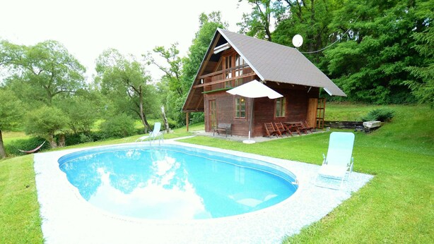 Une cabane en bois avec une piscine, entourée de pelouse et d’arbres.