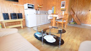 Un salon confortable avec une table basse en verre, un canapé, un coin cuisine équipé d’un four à micro-ondes et une table à manger avec des chaises.