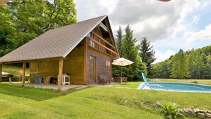 Une cabane en bois avec un toit en pente, une piscine et un patio couvert.