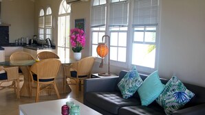 A spacious living area with a dining table, wicker chairs, a sofa with tropical patterned cushions, and a white coffee table. - Sea-view Apartment in Mambo Beach Near Seaaquarium (Willemstad)