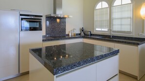 A kitchen with a granite countertop, built-in oven, and a window with blinds. - Sea-view Apartment in Mambo Beach Near Seaaquarium (Willemstad)