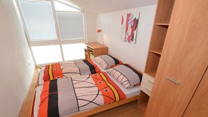 A single bed with a patterned bedspread, a nightstand, a lamp, and a wardrobe in a room with a window and a wall art piece. - South Bohemia Family Escape (Bechyne)