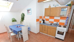 A compact kitchen with a dining area, featuring a tiled floor, wooden cabinets, a stove, and a small sink. - South Bohemia Family Escape (Bechyne)