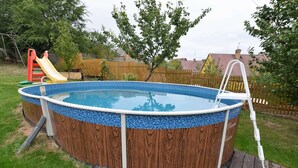 A circular above-ground pool with a wooden exterior and blue mosaic tiles, surrounded by a grassy yard and a wooden deck. - Holiday Home in Forest With Private Pool (Petrohrad)