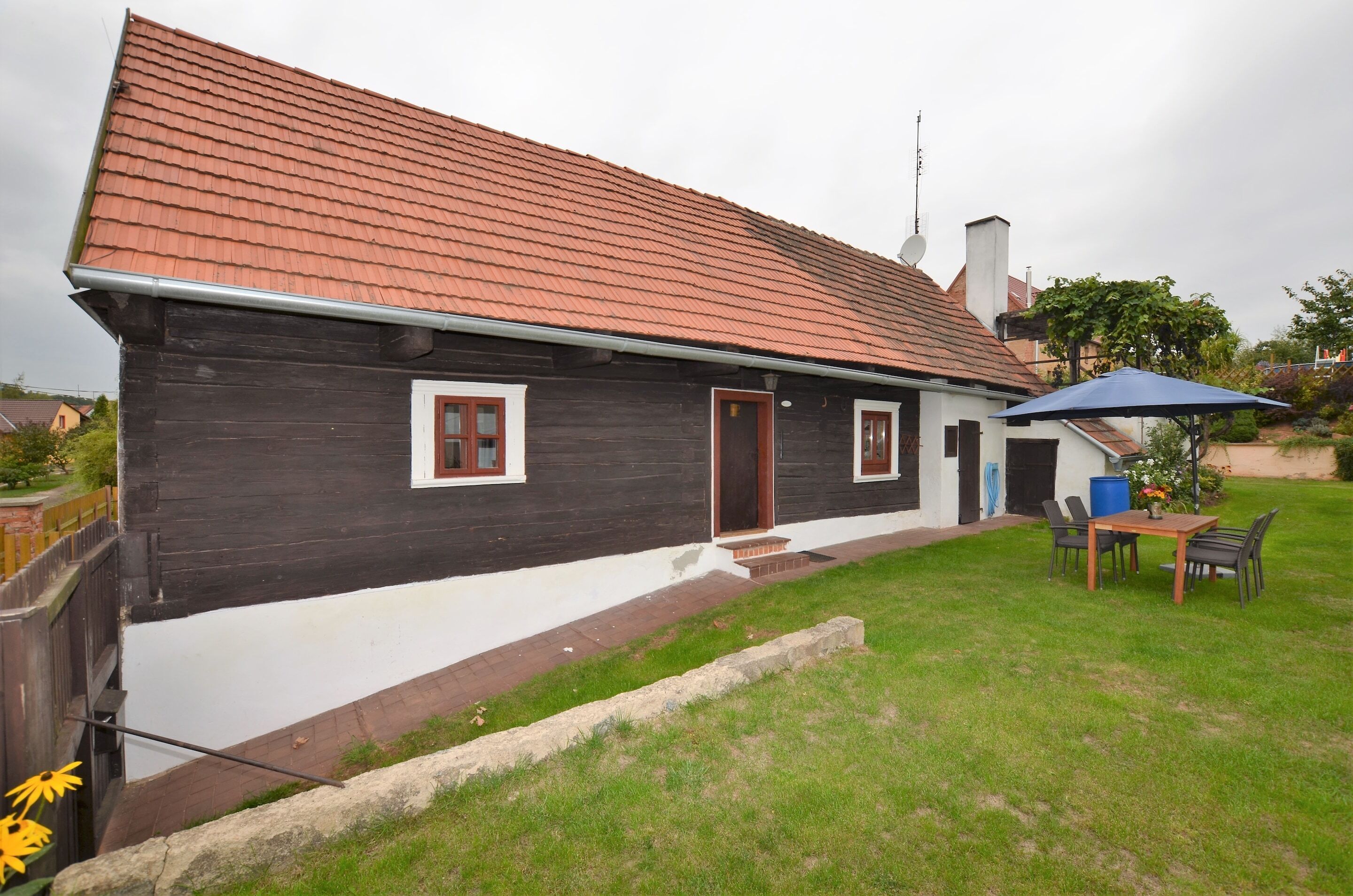A wooden house with a red-tiled roof, a small porch, and a table with chairs outside.