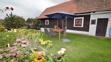 A house with a garden, a table with chairs, and a blue umbrella.
