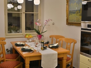 A dining table set with plates, glasses, and a pitcher, surrounded by wooden chairs with red cushions. - Charming Prague Downtown Flat (Prague)